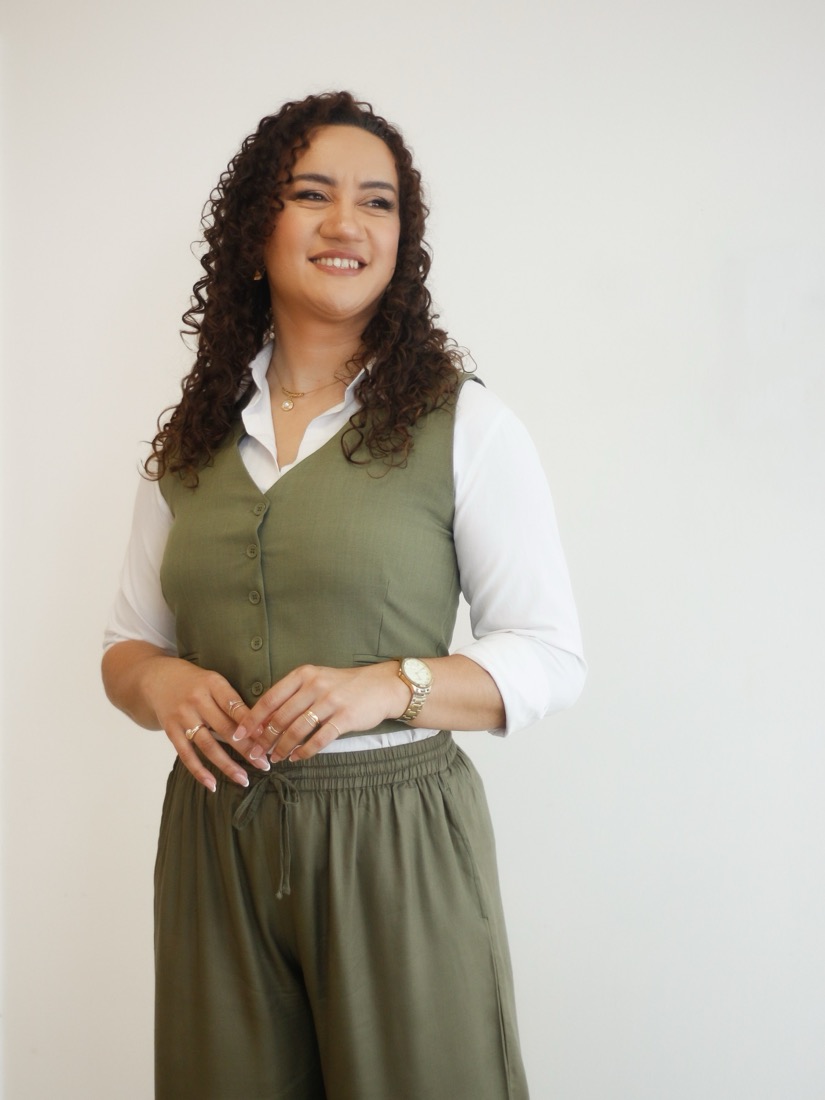 Joyce Leão sorrindo, de colete verde-oliva e camisa branca